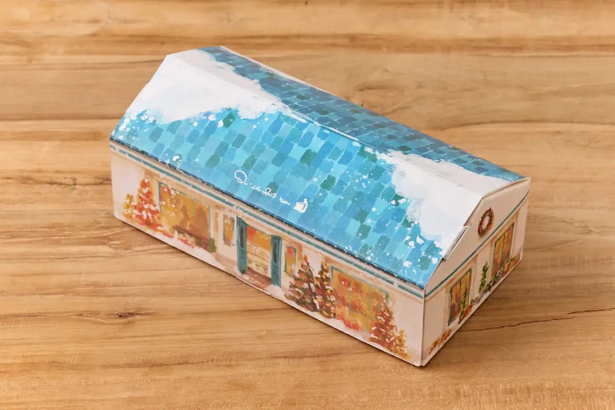 冬のバトンのパッケージ キル フェ ボンのお店が、冬景色をまとって 雪の積もった青い屋根に、あたたかな灯りがともる窓辺とクリスマスツリー。キル フェ ボンの店舗をモチーフにした冬の情景を、そのまま家型BOXに描きました。箱を手にした瞬間から、冬の物語が始まるようなパッケージです。食べ終えたあとも小さなお家として飾っておきたくなる愛らしさで、離れて暮らす大切な方のもとへ、お店の灯りのようなぬくもりを届けます。